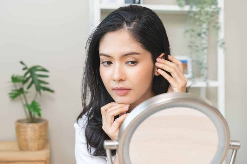 A young woman checks her hair in a mirror. Part of hair health is knowing what the pH level in hair