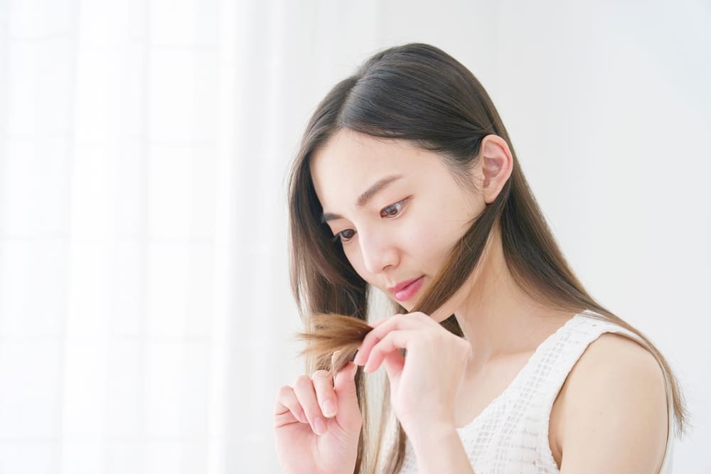An Asian woman checking her hair’s ends. It’s important to maintain a good pH balance in hair.