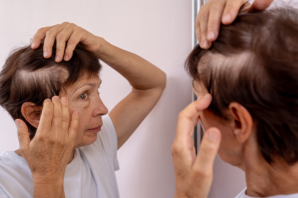Mature woman gently parting her hair in the mirror, noticing aging changes in hair density