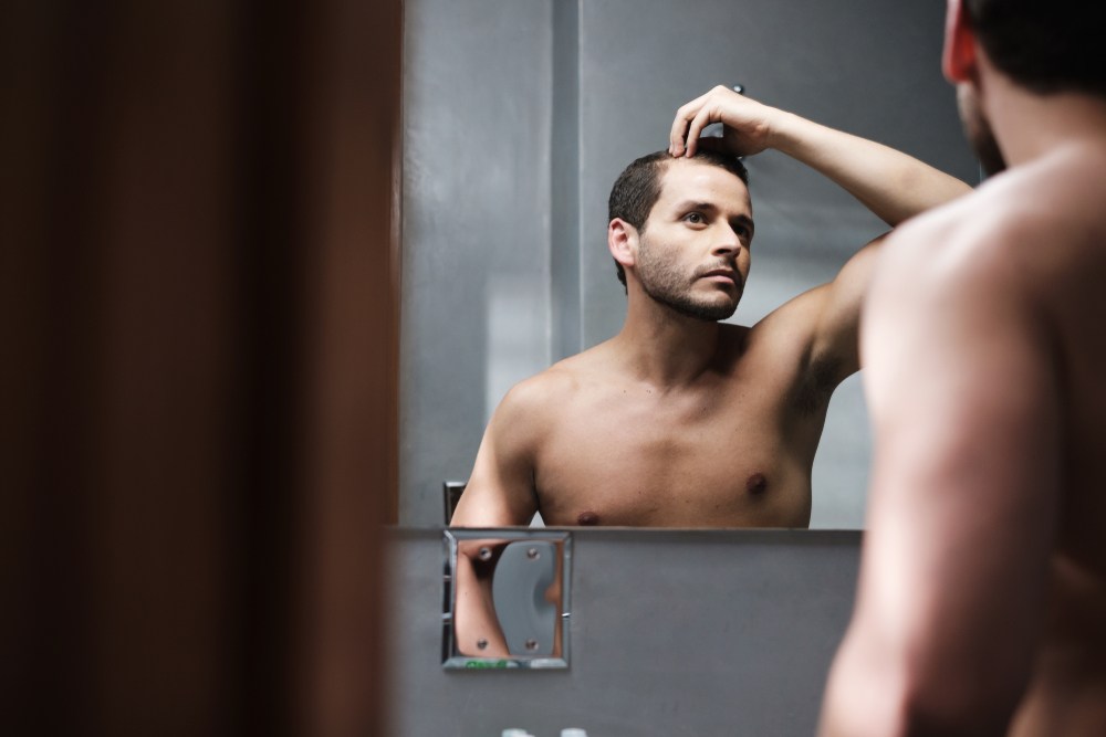 A young man is checking his hair, signaling it may be time for a Norwood scale consultation