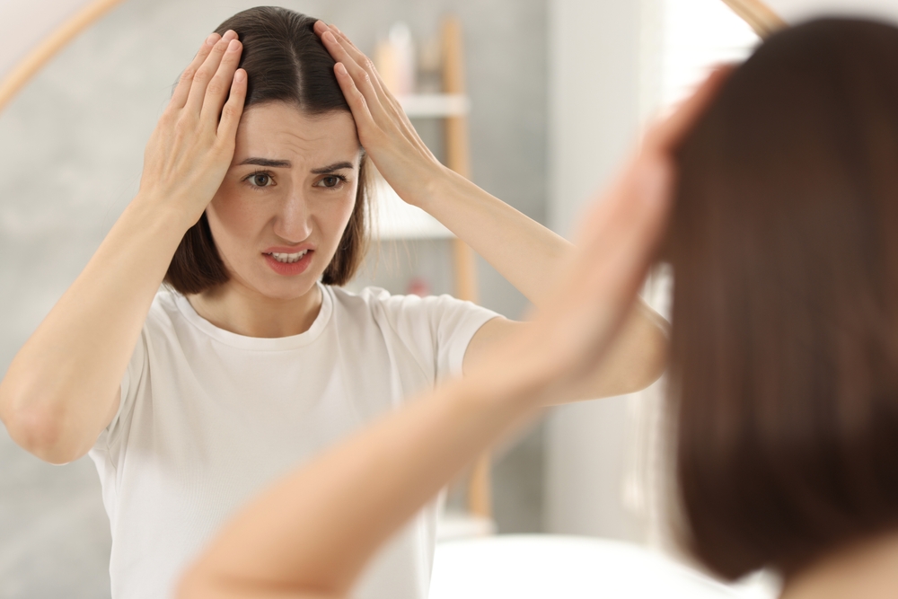 Worried woman checking her thinning hair, a common sign of stress and hair loss