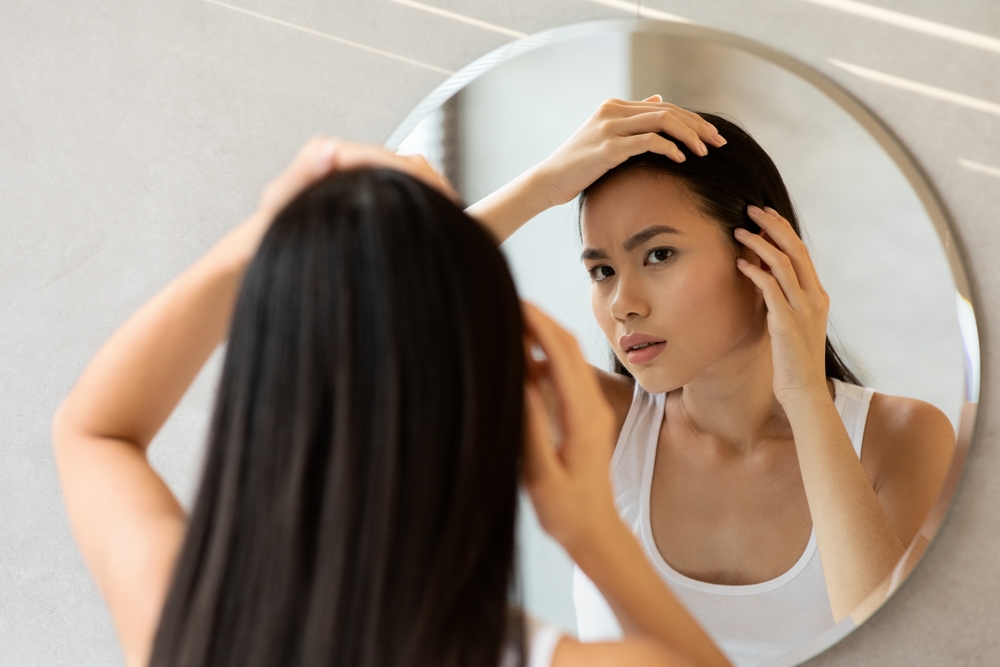 A young woman checks her hair in the mirror. An exosome treatment can do a lot for hair loss.